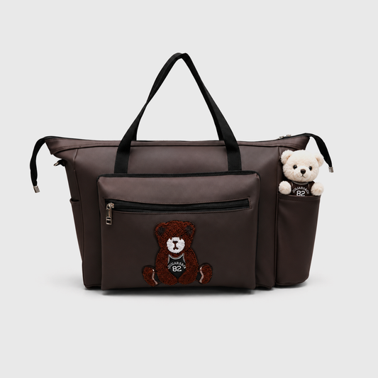 Brown faux leather baby bag with teddy bear embroidery, front zip pocket, spacious interior, and black shoulder handles for stylish daily use.