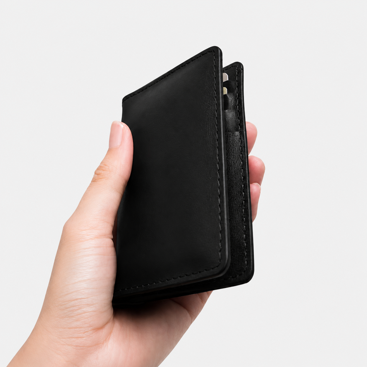 Minimal black leather bi fold wallet displayed on white background with sleek stitching and elegant everyday carry appearance.