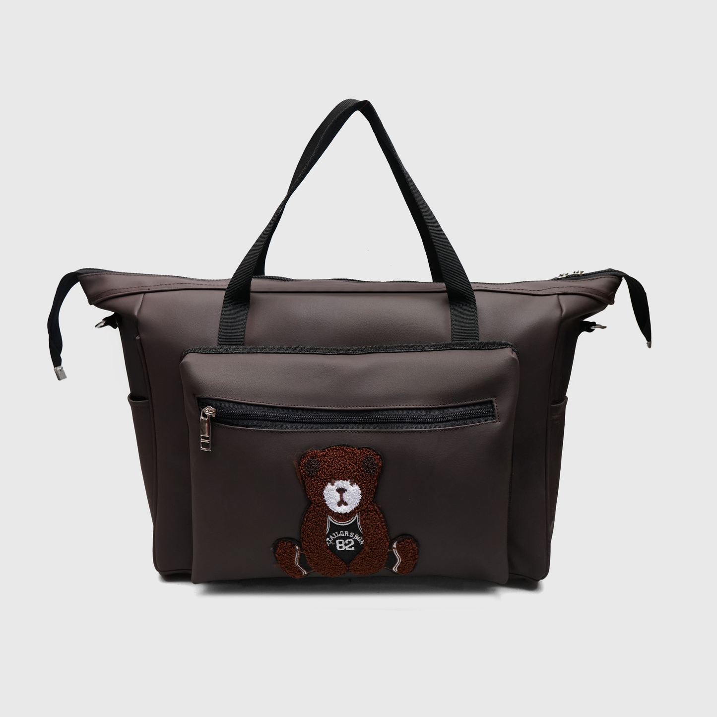Premium diaper travel bag in brown faux leather featuring teddy patch design, secure top zip closure, side pockets, and lightweight carry design.
